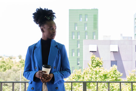 Portrait of smiling young african woman wearing a blue jacket suit and holiding a coffee.