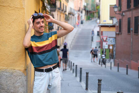 Young caucasian man with long false nails smiling, holding his sunglasses, standing against a yellow wall.の写真素材