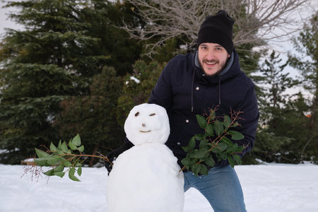 Young caucasian man making a smiley snowman harms with branches.の写真素材