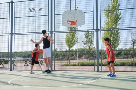 Three brothers playing basketball, one of them has a leg prosthesis.の写真素材