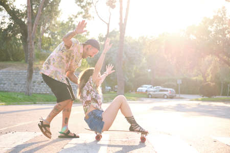 Young cool tattooed couple having fun skateboarding.の写真素材