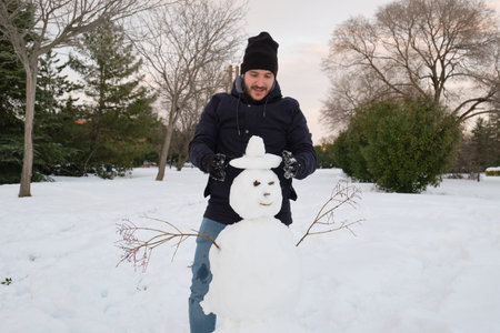 Young caucasian man making a smiley snowman with a hatの写真素材