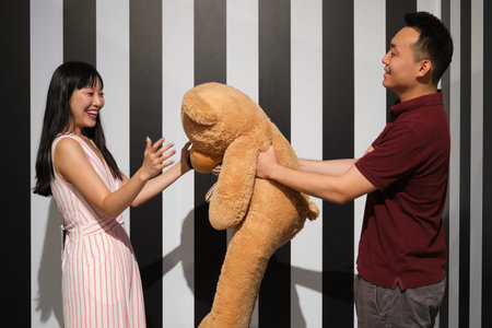 Young asian woman receive a teddy bear from her boyfriend on a striped room.の写真素材