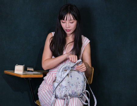 Young asian woman pretending to be a child sit on school desk and open backpack.