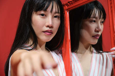 Young asian woman pose with a red framed mirror over a red background.の写真素材