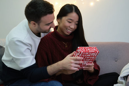Young caucasian man giving a Christmas present to his asian girlfriend.の写真素材
