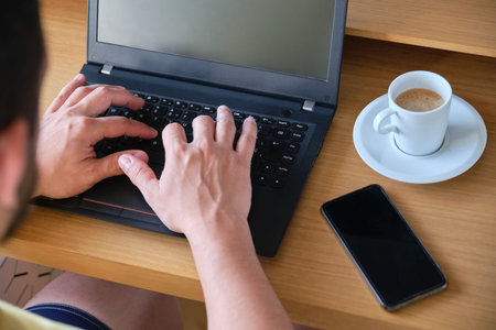 Unrecognizable man working with laptop, smartphone and a cup of coffee.