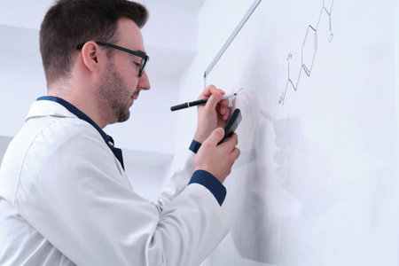 Male researcher in lab coat writing notes on whiteboard.