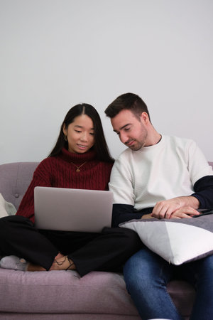 Young couple relaxing on a couch at home using a laptop.