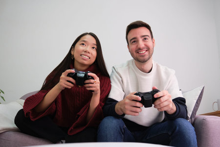 Young multiracial couple playing video games and using joystick controllers.