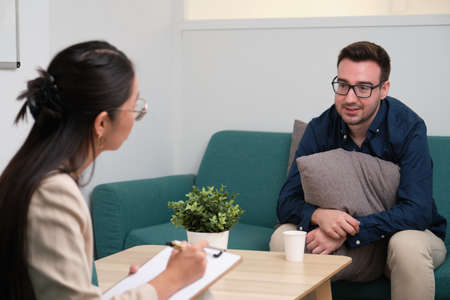 Asian female psychologist and caucasian man patient at therapy.の写真素材