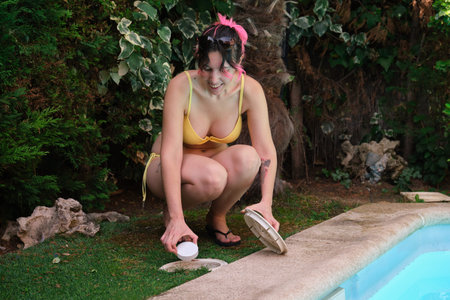 Woman smiling and putting a chlorine tablet into the pool skimmer.