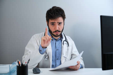 Young doctor looking at camera and talking sitting at desk in a medical office.の写真素材