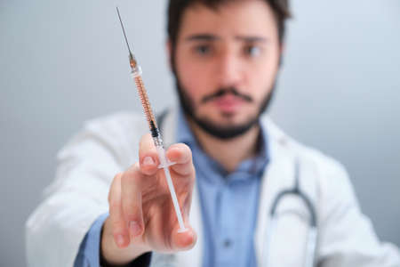Unrecognizable doctor holding a syringe with an orange liquid.の写真素材
