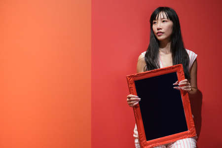 Young asian woman pose with a red framed mirror over a orange background.の写真素材