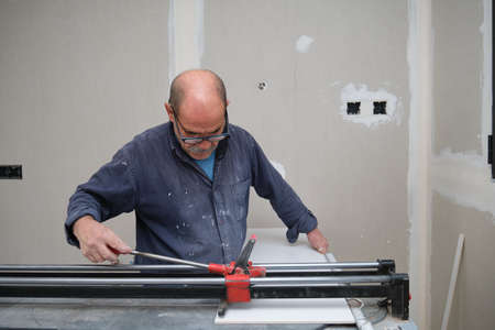 Senior contractor cutting a white ceramic tile with a manual tile cutter.の写真素材