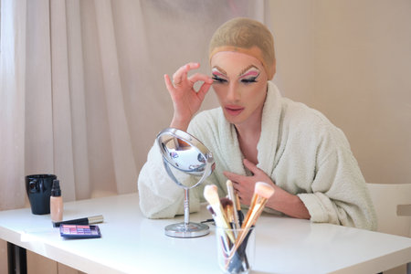 Drag queen person applying false eyelashes and wearing bathrobe.