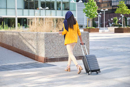 Young indian businesswoman holding a cup of coffee and a suitcase backwards.の写真素材