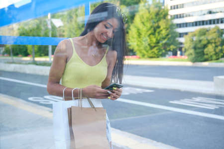 Young latin woman waiting for the bus at a bus stop at street.の写真素材