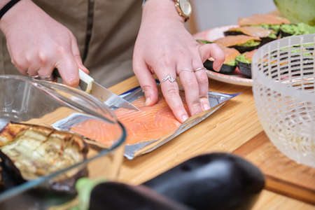 Unrecognizable woman cutting smoked salmon to prepare filled avocados.の写真素材
