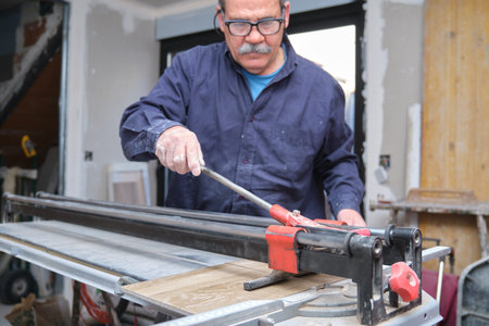 Senior contractor cutting a ceramic wood effect tile with a manual tile cutter.