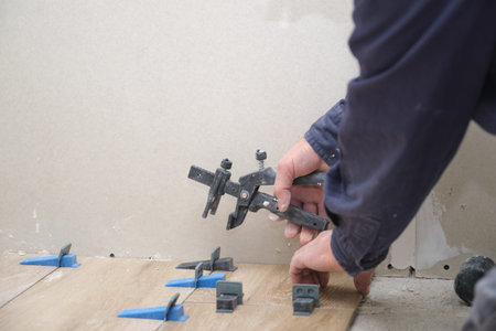 Mason hands adjusting tile levelers between ceramic wood effect tiles.