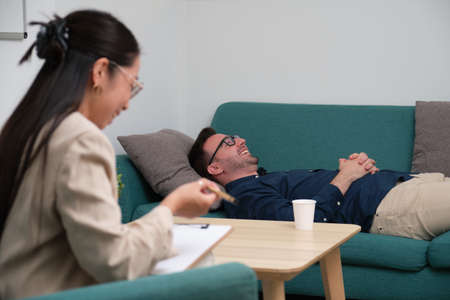 Asian female psychologist and caucasian man patient laughing at therapy.の写真素材