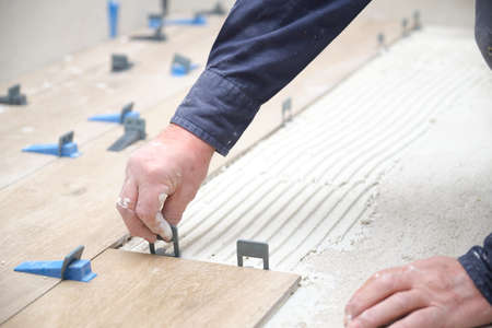 Worker hands laying ceramic wood effect tiles using tile levelers.の写真素材
