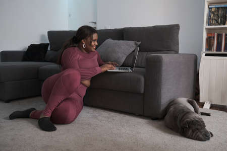 African woman in sportswear sitting on the floor using a laptop at home.の写真素材