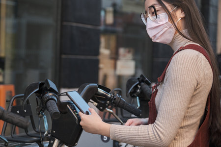 Young asian woman wearing face mask renting a bicycle using the phone app.