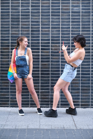 A lesbian couple taking pictures to each other with a smartphone.