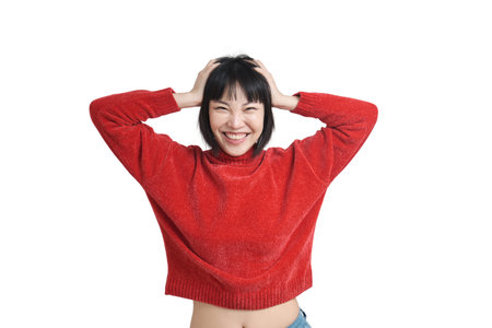 Young asian woman laughing and touching her head with her hands, wearing winter red sweater, isolated on white background.の写真素材