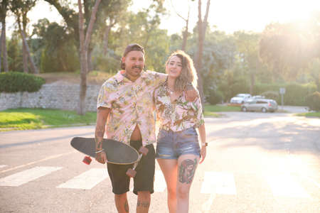 Young cool tattooed couple walking together with a skateboard on a summer sunny day.の写真素材