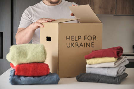 Unrecognizable volunteer filling donation box with warm clothes, jeans, t-shirts to help ukrainian refugees.の写真素材
