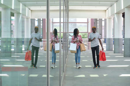 Young black couple drinking refreshing drinks and going shopping, walking outside the shopping center. City life concept.の素材 [FY310184116555]