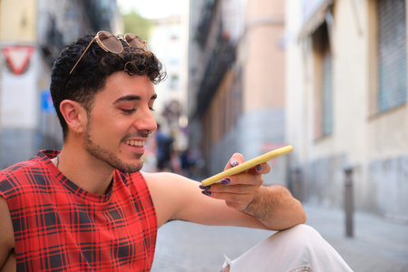 Young caucasian man with long false nails recording an audio note on the smartphone sitting on the...