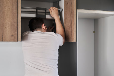 Young latin man installing an accessible kitchen cabinet in the kitchen using a screwdriver. Assembling modern kitchen furniture.の写真素材