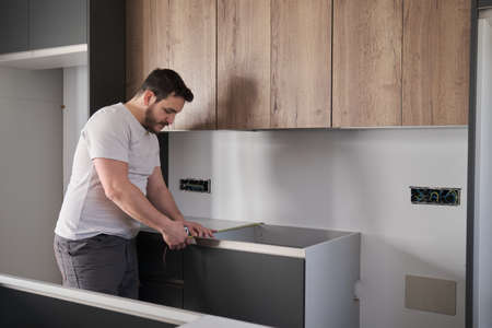Young latin man using measuring tape before placing countertops on modern kitchen.の写真素材
