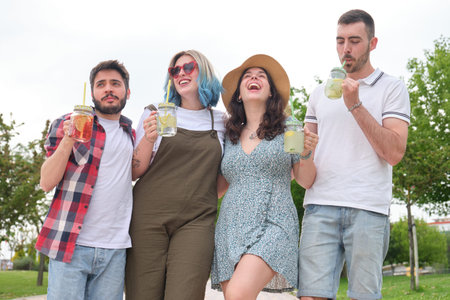 Group of happy friends drinking refreshing drinks and laughing in a park on a sunny summer day.