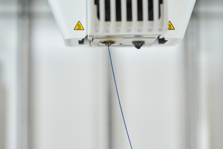 Blue plastic filament extruding through 3D printer nozzle or extruder.の写真素材