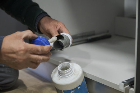 Mature plumber hands applying glue to a grey plastic pipe. Repairman working.の写真素材