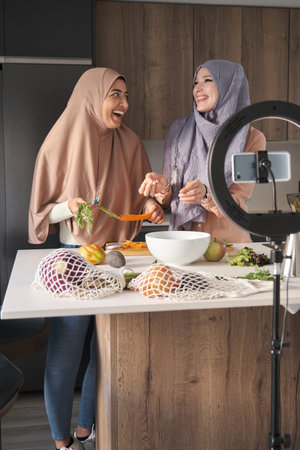 Two muslim food vloggers laughing while preparing a salad at modern kitchen.の写真素材