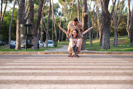 Young cool tattooed couple having fun skateboarding. Boyfriend is pushing his girlfriend on the longboard.の写真素材
