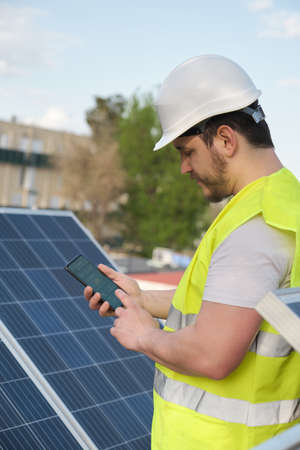 Technician using smartphone app for controlling photovoltaic solar power station. Green eco friendly energy.の写真素材