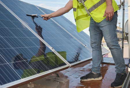 Unrecognizable technician washing solar panels with a squeegee window cleaner.の写真素材