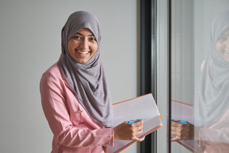 Portrait of young muslim businesswoman smiling wearing hijab in office near by a window.