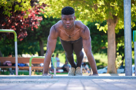 Young fit shirtless black man doing push-ups outdoors on sunny summer day. Fitness and sport...