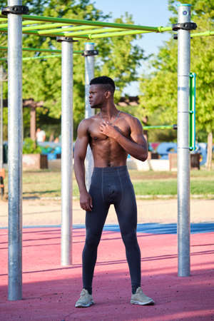 Young fit shirtless black man looking at a side in a calisthenics park outdoors on sunny day. Fitness and sport lifestyle.の写真素材