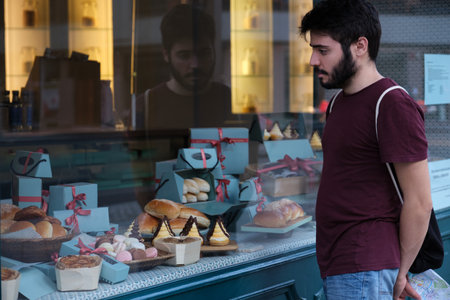 Young man choosing a pastry standing in front of bakery showcase.の写真素材