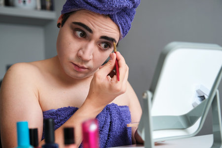 Young drag queen man applying eyeshadow after shower with a towel on his head.